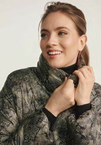 Padded coat wężowy w ciemnozielonych i czarnych odcieniach, z wysokim kołnierzem i ściągaczami. Materiał wydaje się błyszczący z teksturowanymi wzorami.