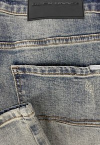 Denim jeans met een lichte wassing, zichtbare stiksels, een achterzak en een gestructureerde zwarte leren patch met "BLCK BNNS" in reliëf.