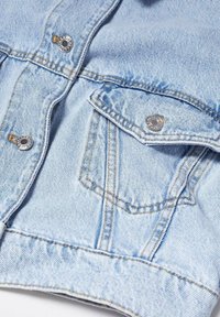 Poche de veste en denim bleu clair avec fermeture par bouton métallique et détails de couture apparents sur tissu texturé.