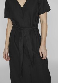 Juodasis mygtukų suknelė su V formos iškirpte, trumpomis rankovėmis ir juosmens juosta. Pagaminta iš lengvos medžiagos, turi lygų paviršių ir paprastą dizainą.