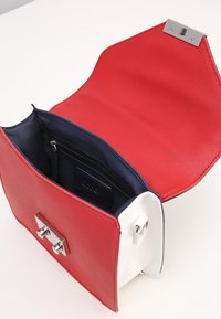 Borsa a mano in pelle rossa e bianca con una texture liscia, ferrature argentate e interno blu navy. Presenta una tasca con cerniera all'interno e una chiusura a patta.