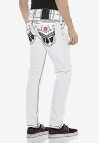Weiße Denim-Jeans mit schwarzen Nähten, ausgestattet mit markanten gestickten Gesäßtaschen in Rot und einem Logopatch am Bund.