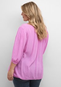 Lyserød bluse lavet af letvægtsstof med en tekstureret overflade, med trekvartærmer, løstsiddende design og samlede detaljer ved manchetterne.