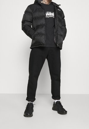 Chaqueta negra acolchada con cierre de cremallera, cuello redondo y patrón acolchado horizontal, combinada con pantalones negros y zapatillas negras.