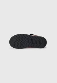 Semelle en caoutchouc noire d'une chaussure Puma avec un motif de bande en vagues, affichant le logo Puma en lettres en relief au centre.