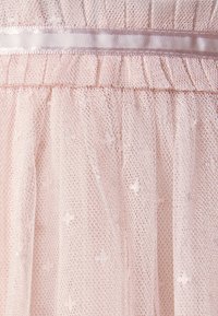 Tissu en tulle rose pâle avec de petites croix brodées et un détail de ruban en satin près du bord supérieur, créant un motif texturé délicat.