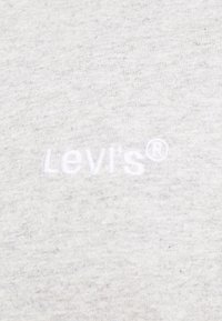 Šedá bavlněná tkanina s vyšitým logem "Levi's" v bílé barvě. Povrch je hladký s mírným melírovým vzorem.