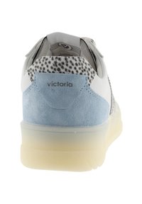 Zapatilla blanca y azul claro con cuello del talón moteado y suela translúcida, vista desde atrás mostrando el logo "victoria".