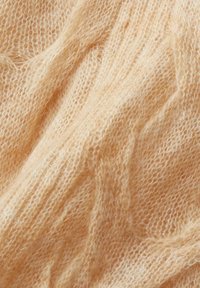 Tissu beige doux et duveteux en tricot avec un tissage lâche et aéré et des fibres texturées visibles.