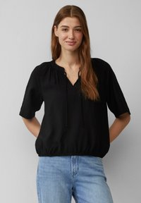 Haut noir à manches courtes avec une coupe décontractée, doté d'un col rond et d'un cordon de serrage à l'avant, fabriqué dans un tissu léger.