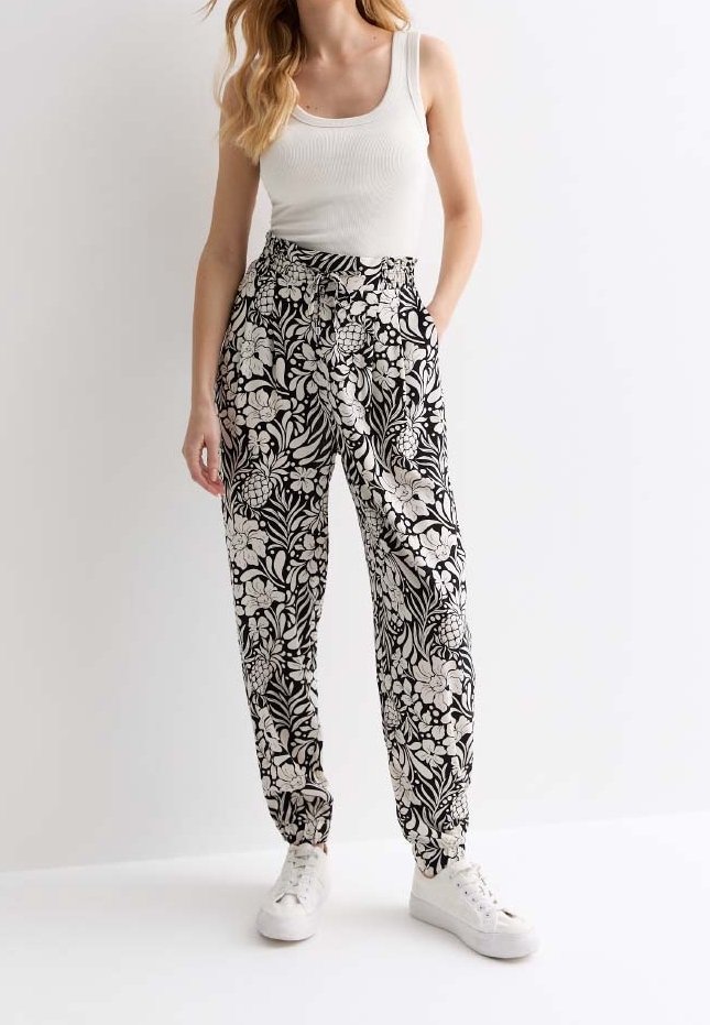 Pantalons à motif floral noir et blanc avec une taille élastique, poches latérales et poignets aux chevilles, associés à des baskets blanches.