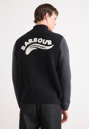 Pull en laine bleu foncé et gris avec un col montant. Il présente un logo "Barbour International" blanc distinctif à l'arrière. Tissu en tricot texturé.