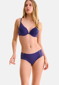 Paarse lingerieset met een textured, gewatteerde beugelbh met golvende randen en een hooglopende onderkant met gestreepte accenten en strikjes.