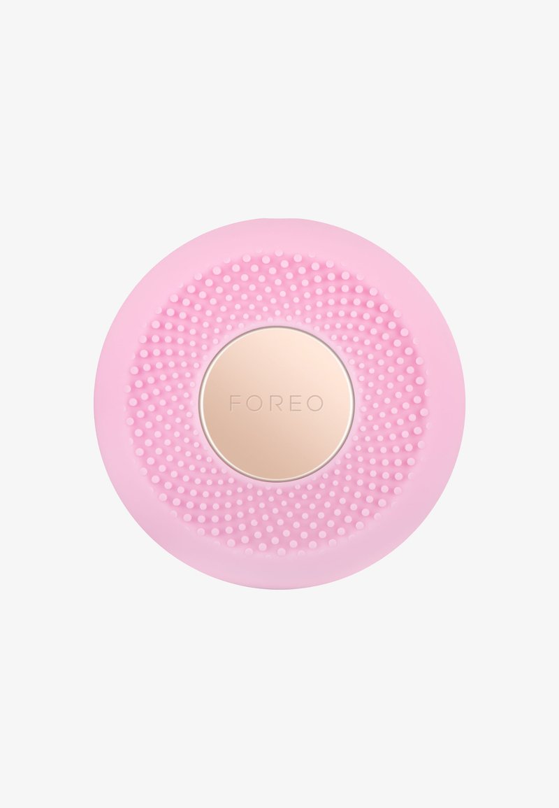 Roze siliconen gezichtsreinigingsapparaat met een gestructureerd, geperforeerd oppervlak en een gouden logo in het midden. Circulaire vorm, compact ontwerp.