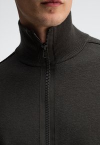 Dunkelgrauer Reißverschluss-Pullover mit hochgeschlossenem Kragen, strukturiertem Rippenhals und glattem Stoff. Verfügt über einen schwarzen Reißverschluss zum Schließen.