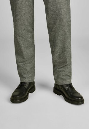 Schwarze Lederschuhe mit strukturiertem Finish und Kappenzehen, kombiniert mit hellgrauen strukturierten Hosen, beide von der Taille abwärts gezeigt.