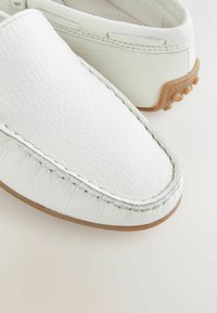 Biele kožené slip-on topánky s textúrovaným povrchom, kontrastným prešívaním a gumovou podrážkou. Okrúhla špička a subtílne dizajnové detaily na exteriéri.
