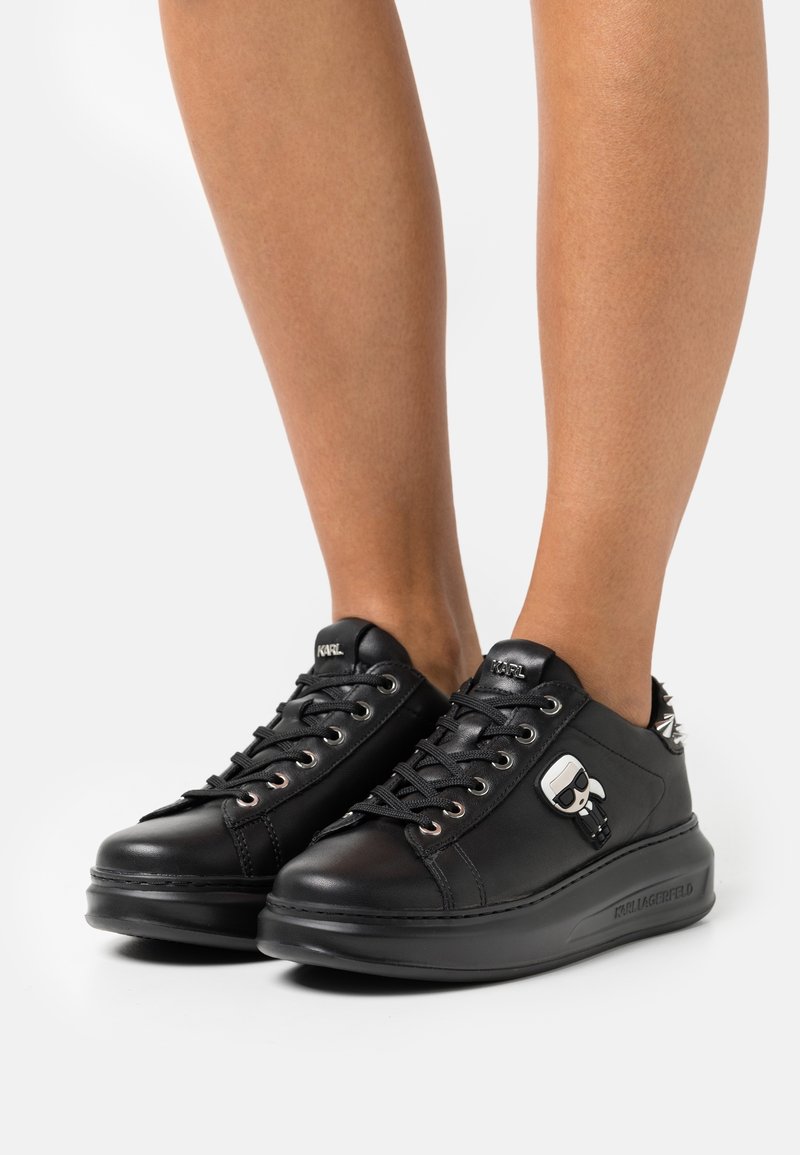 Baskets en cuir noir avec un design à lacets, œillets métalliques, semelle en caoutchouc et un accent de caractère unique sur le côté. Fini texturé.