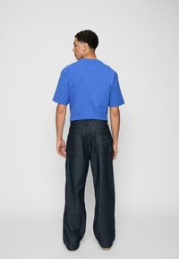 Blå bomulls-T-skjorte med korte ermer, kombinert med mørke denim vide bukser, med baklommer og broderte detaljer.