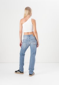 Asymmetrisk hvit ribbet crop topp kombinert med lyseblå straight-leg jeans. Har en brun logo-patch bak, samt svart-hvite stripete sko.