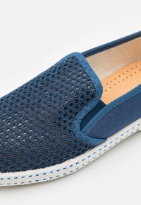 Marine instappers met een mesh bovenwerk, stoffen accenten en een gestructureerde, witte zool met blauwe stiksels. Het interieur is voorzien van perforatiedetails.