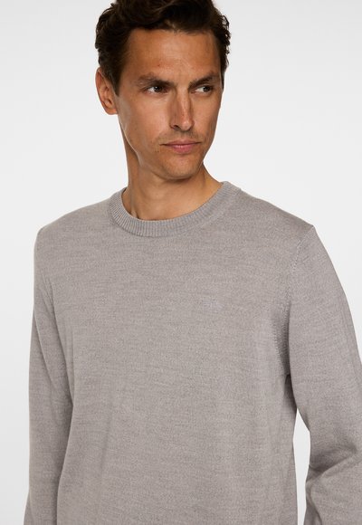 Vaalea harmaa neulepaita, jossa on pyöreä kaula-aukko. Paidan rintamuksessa on hillitty logo ja hihansuissa ribbikuviointi. Paita on sileä ja istuva.