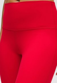 Primer plano de una persona que lleva leggings de tiro alto, de un vibrante rojo, con detalles de costura visibles.