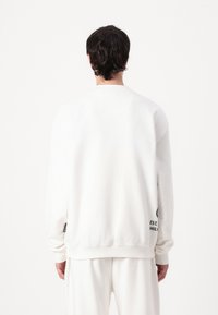 Hvid sweatshirt med en afslappet pasform, ribbet rund halsudskæring og lange ærmer. Har logo-detaljer ved kanten og en blød fleece-tekstur.