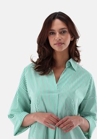 Green and white striped blouse with a V-neck and 3/4 length sleeves, made of a smooth, lightweight fabric. Features a relaxed fit.