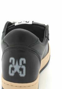 Sneaker nera in pelle con suola beige, caratterizzata da un retro testurizzato e un logo bianco che mostra il numero "26" e un design a stella.