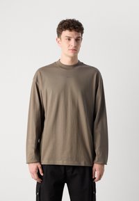 T-shirt à manches longues kaki en coton doux avec un col rond. Doté d'un branding subtil sur la poitrine et d'une coupe décontractée.
