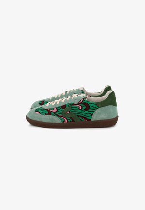 Paire de baskets basses en daim vert, avec un motif abstrait multicolore, des lacets blancs et des semelles en caoutchouc marron sur fond blanc.