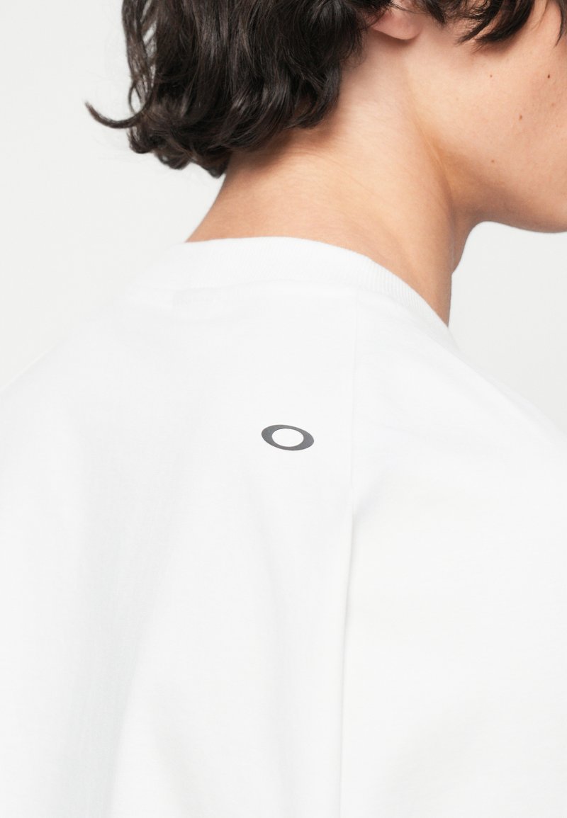 T-shirt blanc en coton, avec un col rond et un petit logo noir à l'arrière près de l'encolure. Texture lisse.