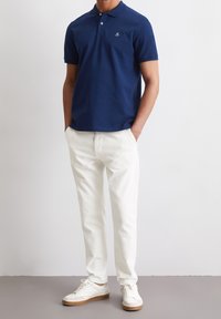 Námořnické polo tričko s límečkem a třemi knoflíky, v kombinaci s bílými džínovými kalhotami a bílými teniskami s světle hnědými podrážkami.