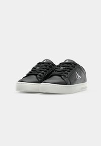 Zapatillas negras de cuero con acabado suave, suela de goma blanca y costuras en tono. Presenta detalle de logo en el costado y diseño clásico de cordones.