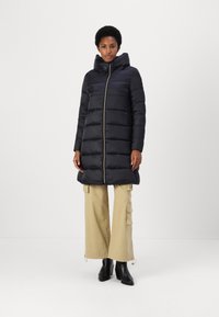 Black puffer coat with a hood, zippered front, and horizontal quilted design. Paired with beige cargo pants and black ankle boots.