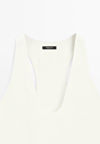 Haut blanc sans manches avec un profond décolleté en V et une étiquette noire indiquant « Massimo Dutti Made in China » à l'intérieur du col.