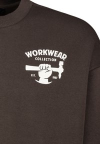 Brown cotton sweatshirt featuring a white graphic logo of a hand holding a hammer. Text includes "WORKWEAR COLLECTION" and "EST. 1987."