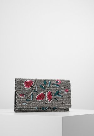 Obdélníková kabelka typu clutch pokrytá stříbrnými korálky s výšivkou růžové růže a zeleného listu, ležící na bílém povrchu.