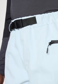 Světlé modré kalhoty vyrobené z hladké, lehké tkaniny. Obsahují elastický pás se černým nastavitelným opaskem a kapsu na zip.