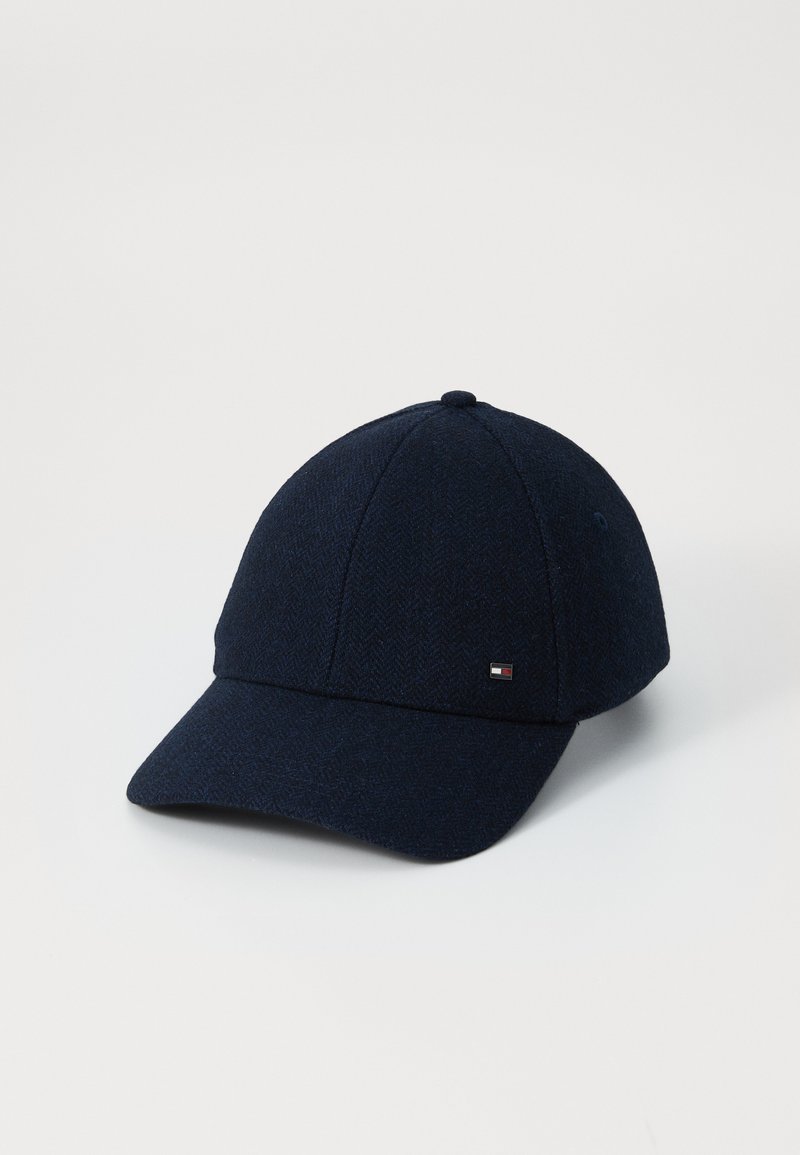 Navy blue cap made of herringbone fabric, featuring a curved brim and a small logo accent on the side. Structured design and smooth texture.