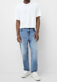 Camiseta blanca corta combinada con jeans rectos de un azul claro y zapatillas blancas. Los jeans presentan un lavado desgastado y un diseño clásico de cinco bolsillos.