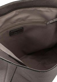 Interieur van een bruine, gestructureerde leren handtas met een gladde, lichte stofvoering. Bevat een ritsvak aan de achterkant voor opbergruimte.