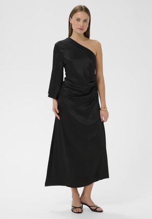 Fekete egylábas maxiruha drapériás kialakítással, puha, sima textúrával. Kiemelve egy széles ujjú résszel és minimalista szandálokkal.