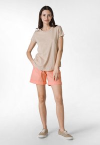 T-shirt beige a maniche corte abbinato a pantaloni corti corallo con orli arrotolati e tasche, indossato con sneakers beige stringate.