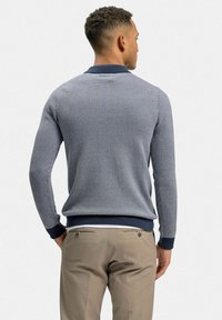 Marinblått stickat tröja med ett strukturerat mönster, med en polo-krage och ribbade ärmslut, i kombination med ljusbeiga byxor.