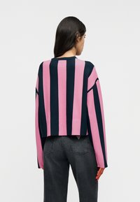 Κοντή μπλούζα με έντονες ροζ και ναυτικές ρίγες, μακριά μανίκια, ριμπ λαιμόκοψη και μικρό ταμπελάκι με λογότυπο στο πίσω μέρος του τελειώματος.