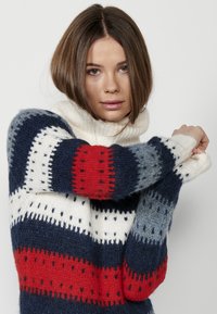 Pull en tricot avec des rayures bleu marine, blanc, rouge et gris, doté de motifs texturés. Design à col montant avec des poignets et un ourlet côtelés. Matière douce.