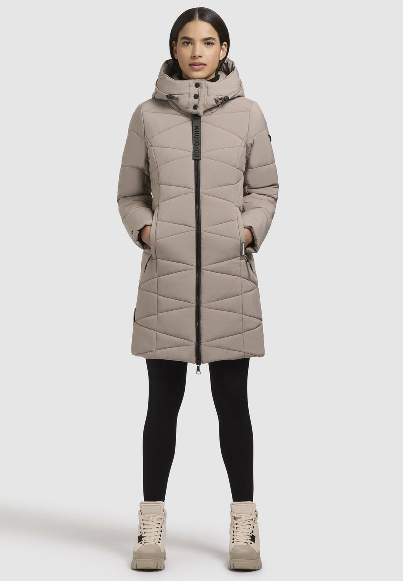 Beige vadderad vinterjacka med huva, med en framficka, triangulärt quiltat mönster, sidofickor och svarta detaljer.