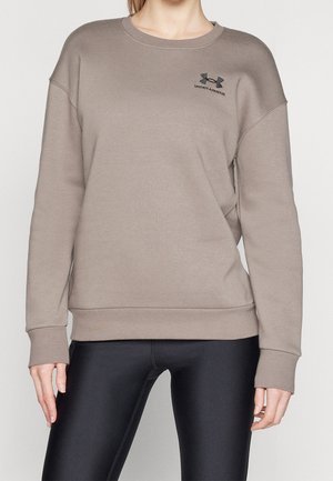 Kvinde iført taupefarvet Under Armour sweatshirt med logo på brystet og sorte tætsiddende leggings, vist fra hals til hofter.